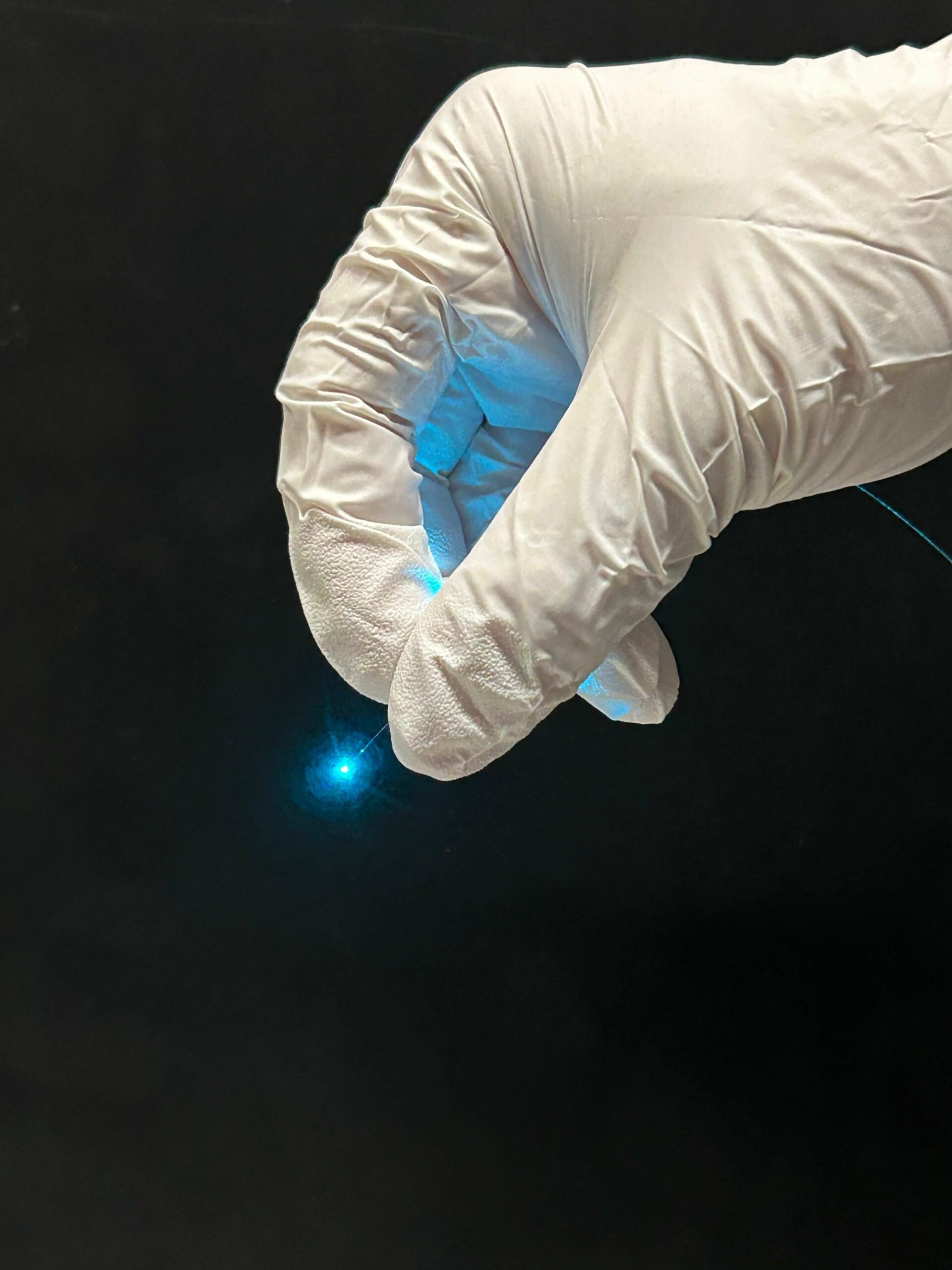 Gloved hand holding an optical fibre emitting blue light, representing DeepEn’s holographic endoscope technology.